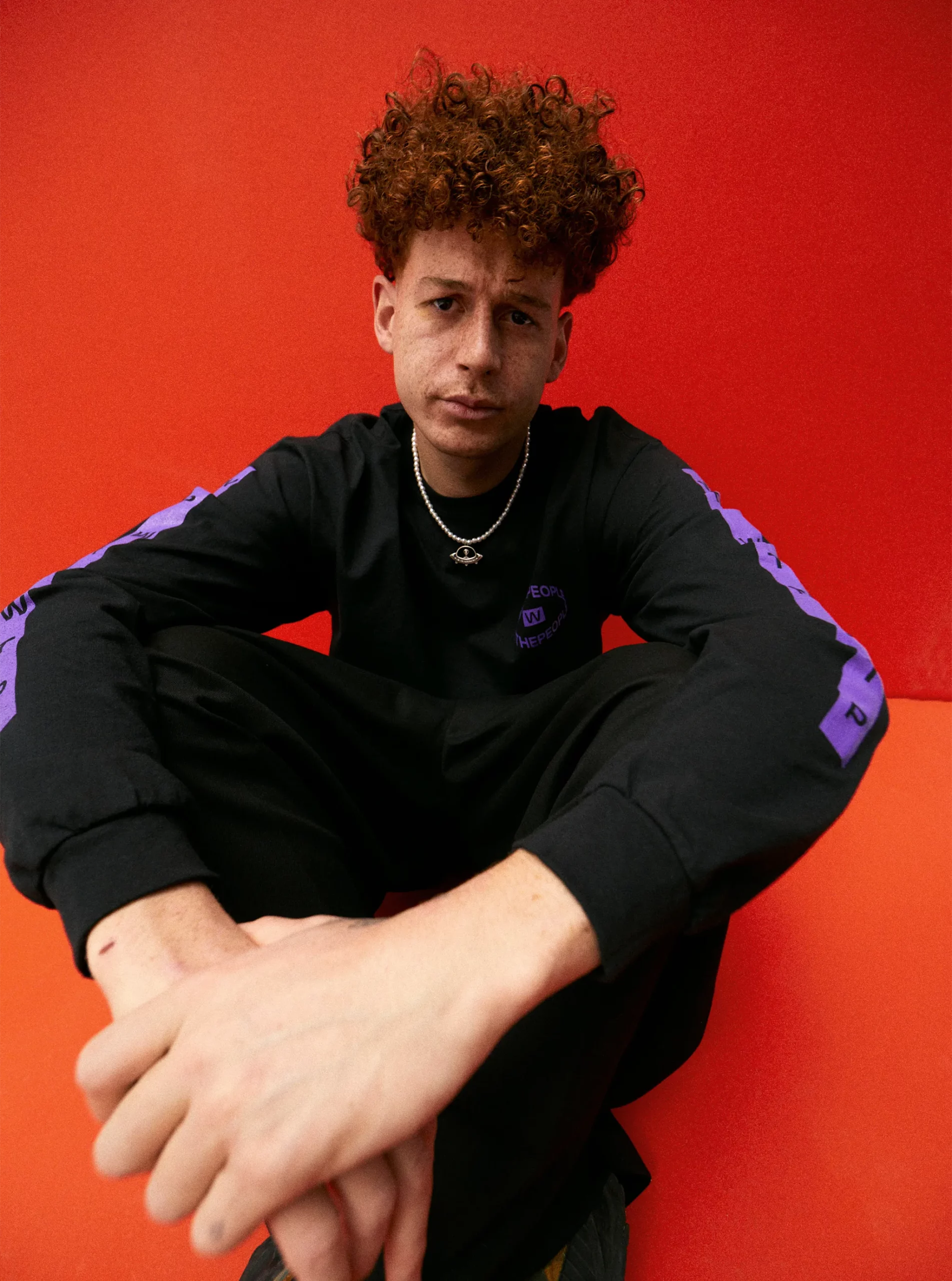 Mann mit Sommersprossen und Locken sitzt auf rotem Boden / Man with freckles and curls sits on red floor